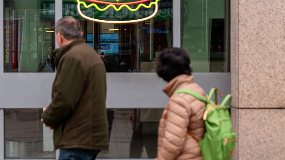 Two pedestrians pass a burger restaurant.