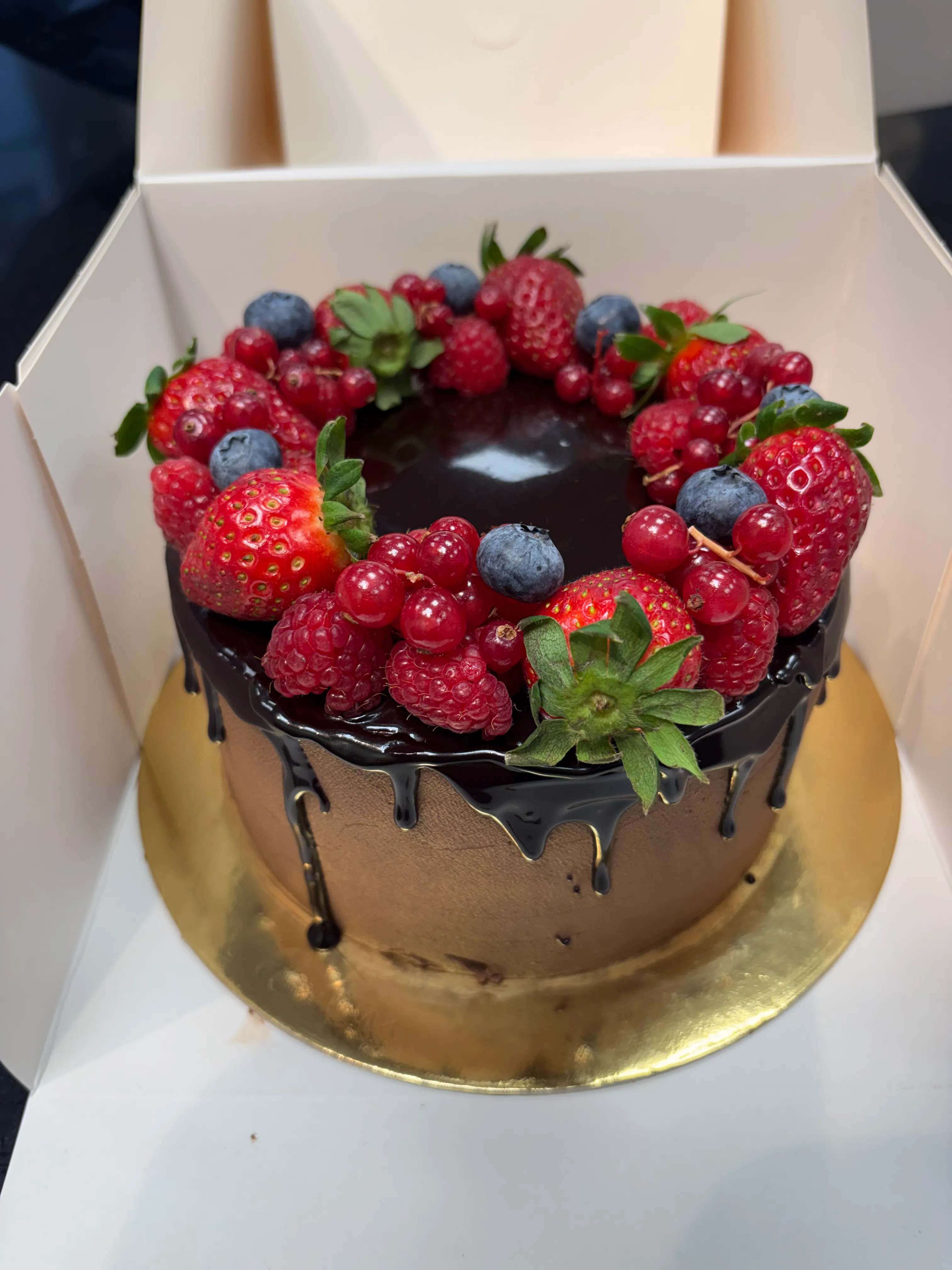 Schokoladenkuchen mit Beeren in weißer Schachtel.