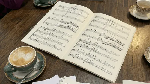 Open sheet music on wooden table with coffee.