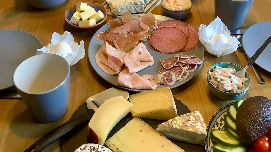 Breakfast table with cheese, bread, fruits, and tea.