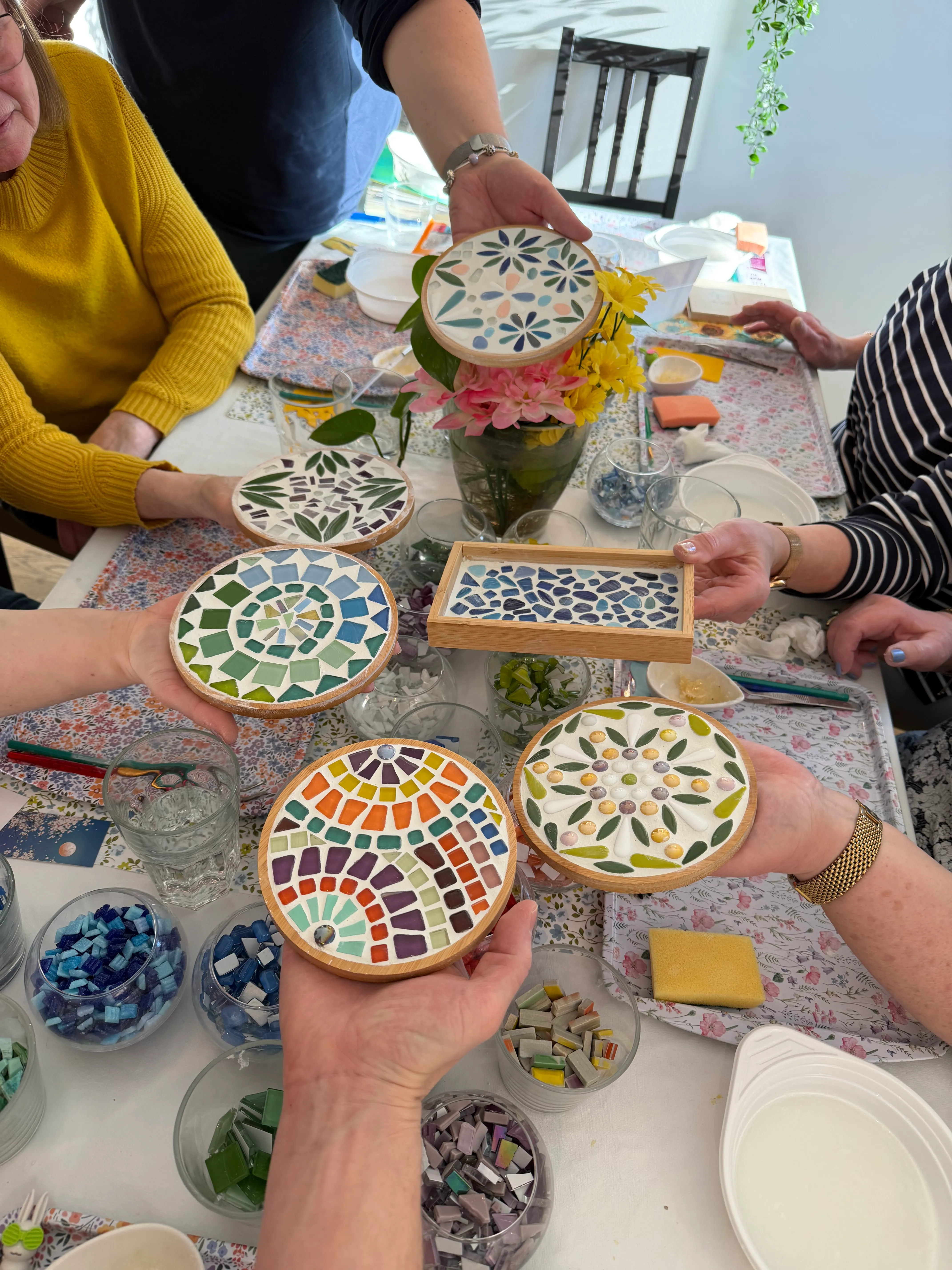 Personen halten bunte Mosaikuntersetzer am Tisch.