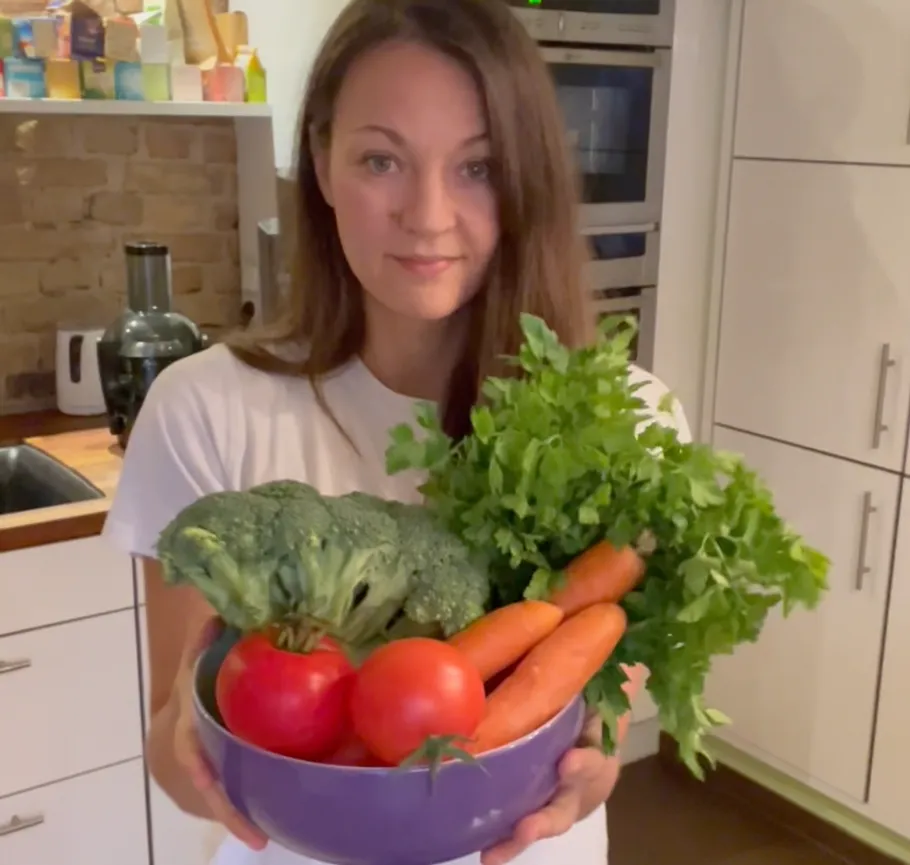 Woman holds bowl of vegetables in kitchen.