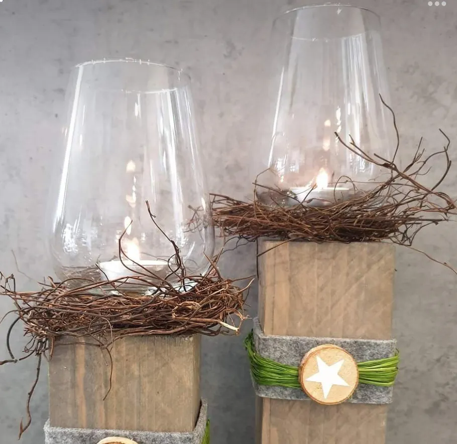 Glaskerzenhalter auf Holzblöcken mit Zweigen.
