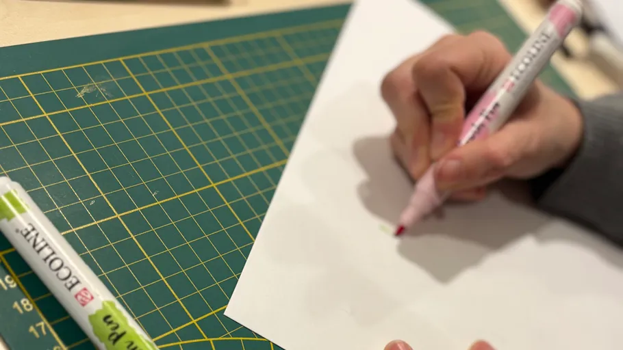 Hand using marker on white paper, cutting mat.