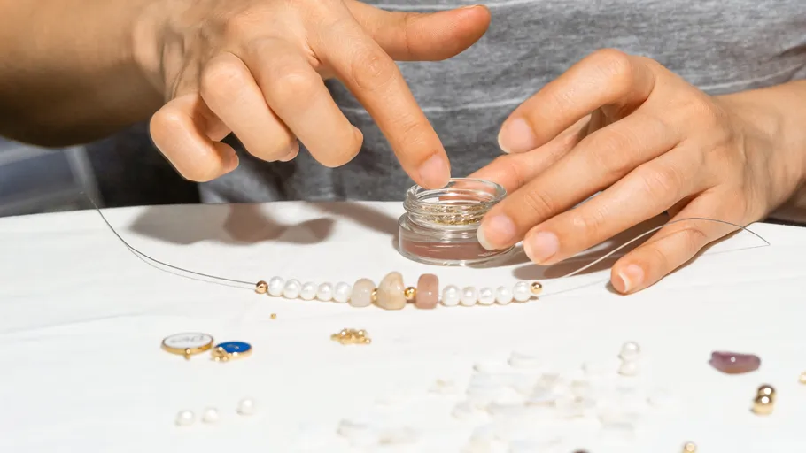 Hands stringing beads on a white table.