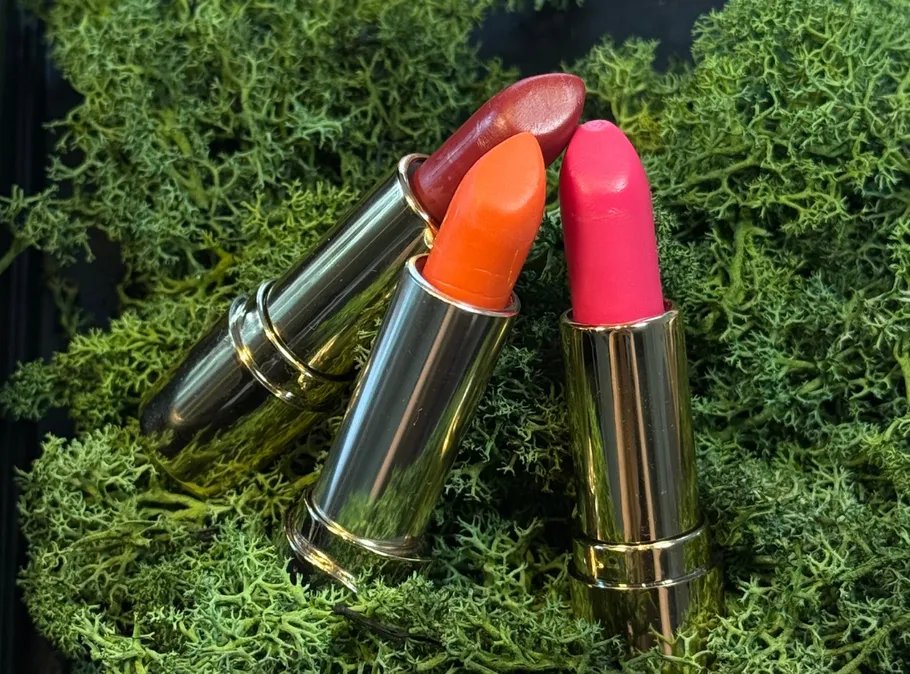Three lipsticks on green moss background.