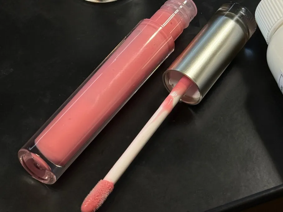 Pink lip gloss with applicator on table.