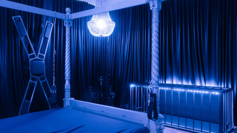 Blue-lit room with bed, chandelier, and cage.