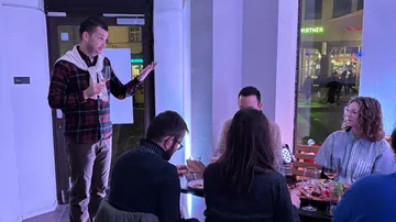Mann steht, spricht zu sitzenden Personen drinnen.