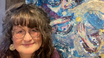 Smiling woman beside colorful abstract painting.