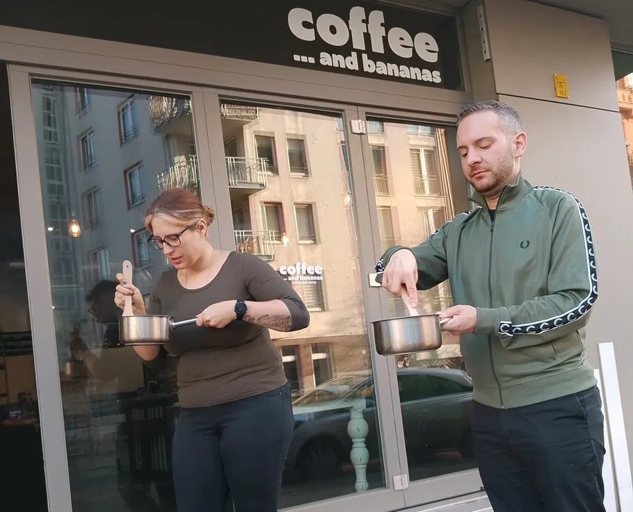 Two people stirring pots outside cafe.