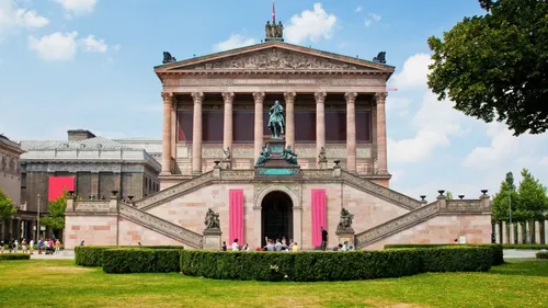 Neoclassical building with steps, surrounded by greenery.