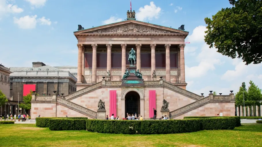 Neoclassical building with steps, surrounded by greenery.