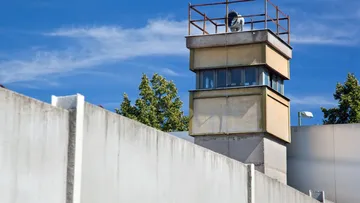 Watchtower overlooking prison wall under blue sky.