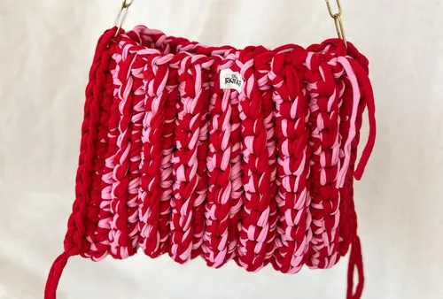 Red and pink knitted handbag suspended indoors.