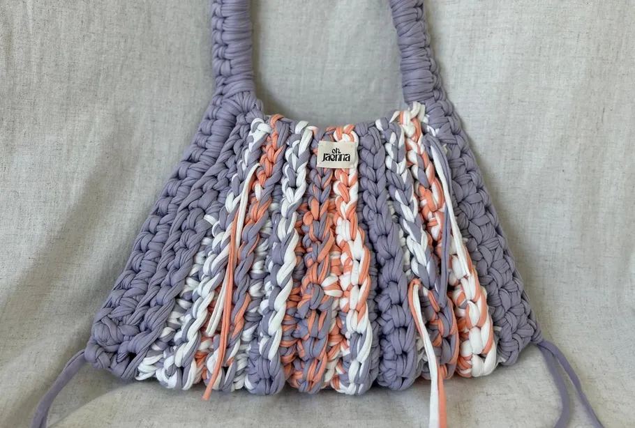 Crocheted bag with colorful stripes, fabric background.