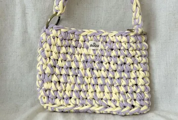 Geflochtene Handtasche mit Henkel auf grauem Hintergrund.