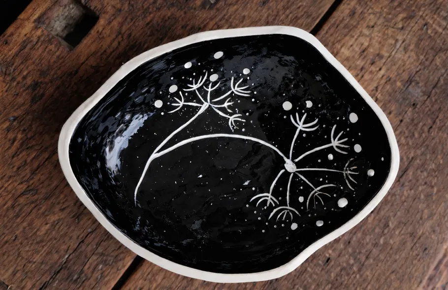 Schwarze Keramikschale mit Löwenzahnmuster auf Holz.