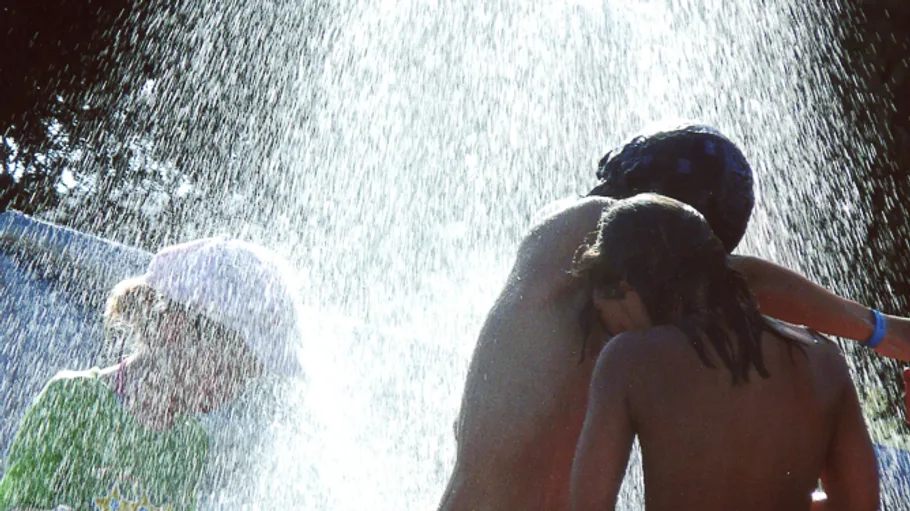 Drei Kinder spielen unter Brunnenwasser.