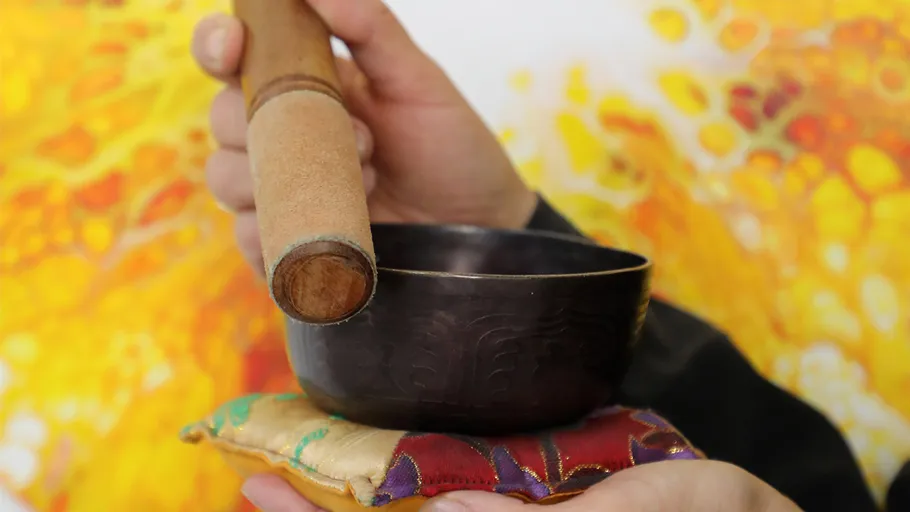 Singing bowl held with wooden mallet against colorful background.