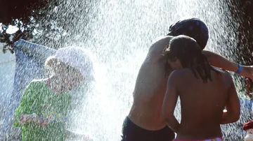 Kinder spielen unter Wasserspray im Freien.