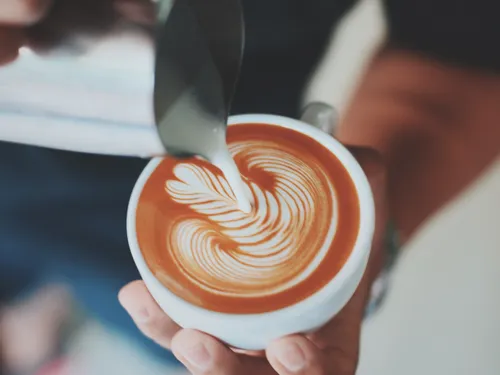 Cup of coffee is decorated with milk foam. Hands visible.