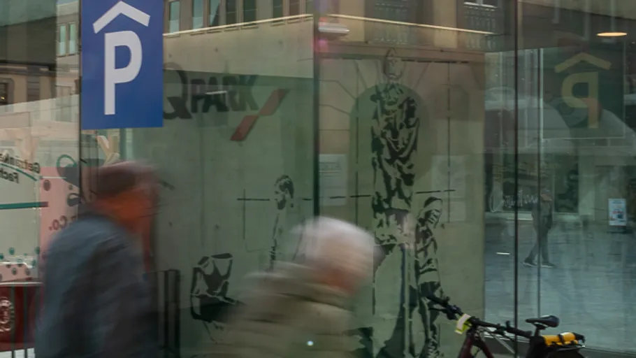 Blurred pedestrians pass glass structure in city.