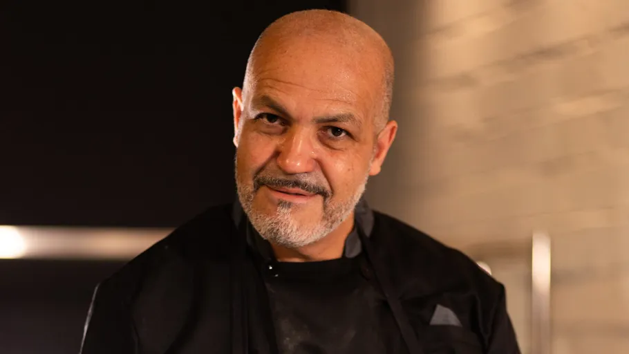 Bald man smiling in dimly lit room.