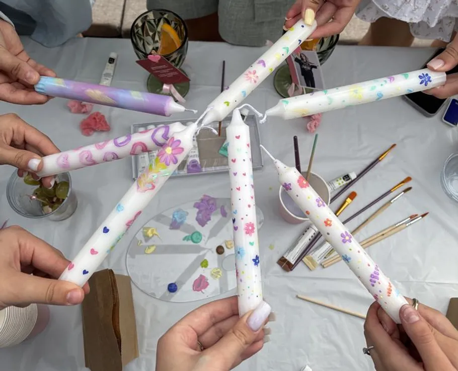 People hold decorated candles at a table.