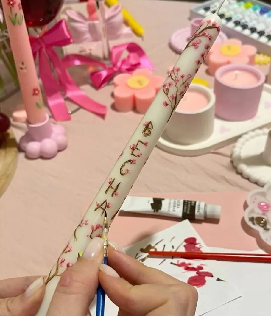 Hand painting floral designs on white candle.