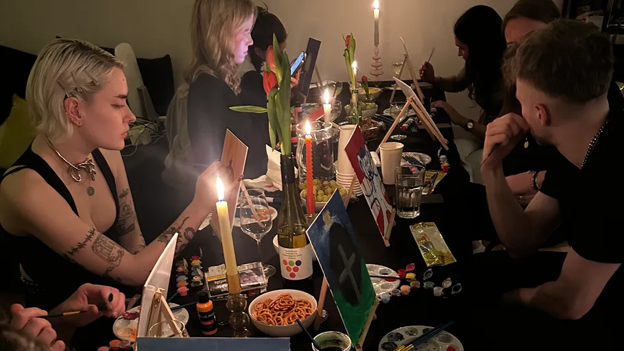 Gruppe von Menschen malt in kerzenbeleuchtetem Raum.