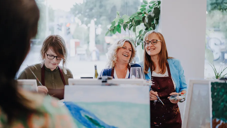 Three women painting, smiling indoors.