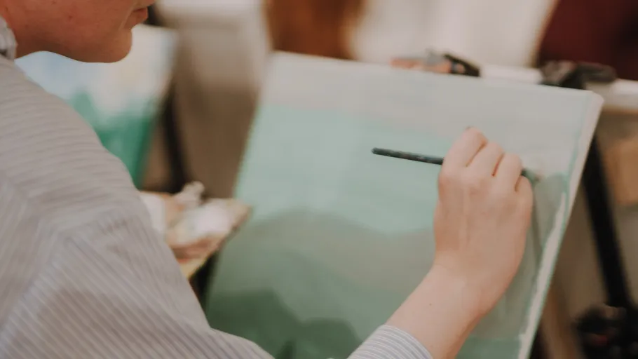 Person painting landscape on canvas indoors.