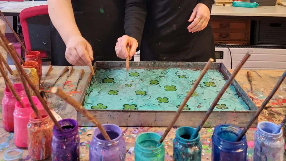 Two people marbling paper with paint trays.