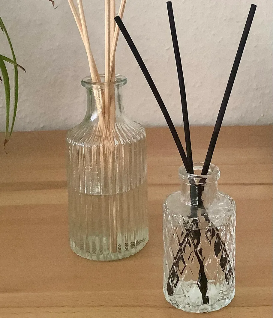Zwei Glasflaschen mit Duftstäbchen auf Tisch.