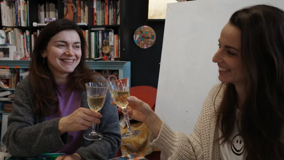 Two women smiling, clinking glasses in a library.