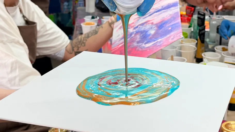 Person pouring colorful paint on canvas.