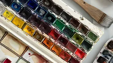 Bunte Aquarellpalette mit Pinsel in der Nähe.