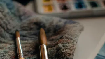 Paintbrushes on textured cloth near watercolor palette.