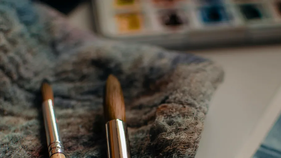 Pinsel auf strukturiertem Tuch neben Aquarellpalette.