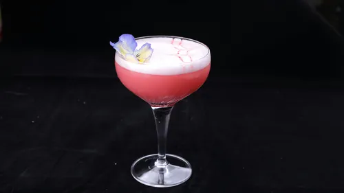 Rosa Cocktail mit Schaum und Blütendekoration.