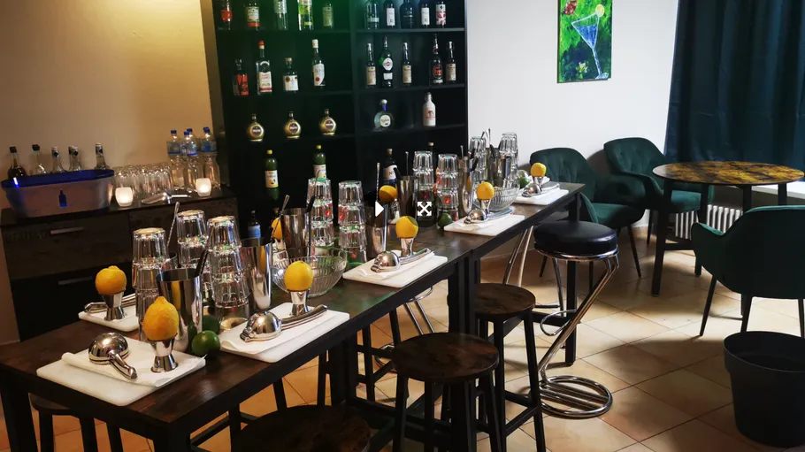 Bar-Einrichtung mit Hockern, Flaschen und Cocktailzubehör.