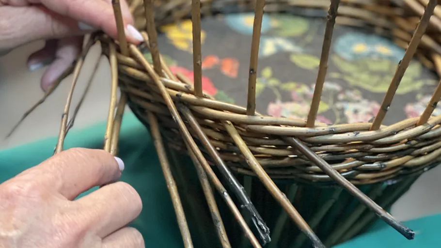 Hands weaving a wicker basket tightly.