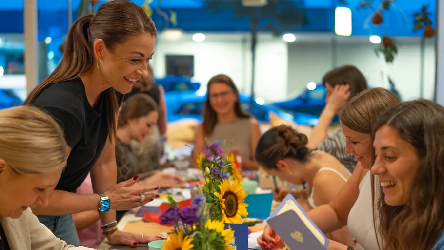 Frauen lachen und basteln an einem Tisch.