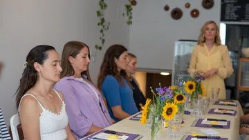 Frauen meditieren an Tisch mit Blumen.