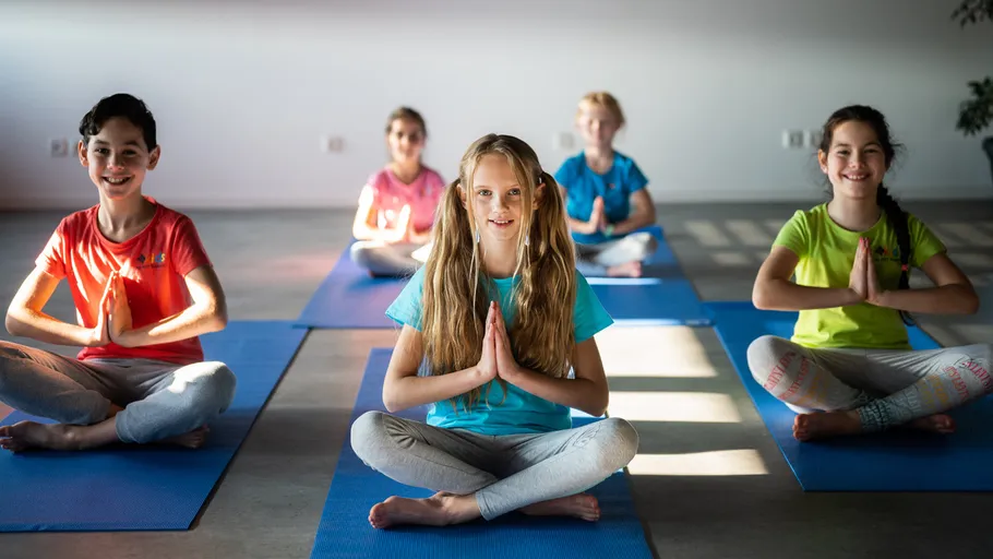Kinder praktizieren Yoga auf blauen Matten drinnen.
