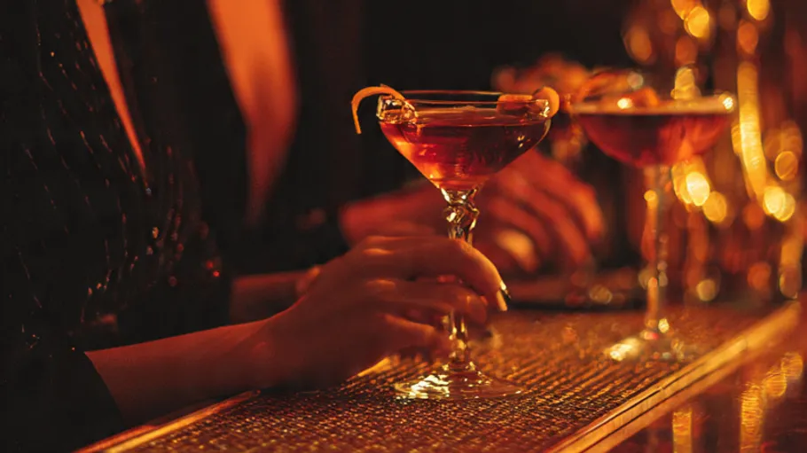 Hands holding cocktails in dimly lit bar.