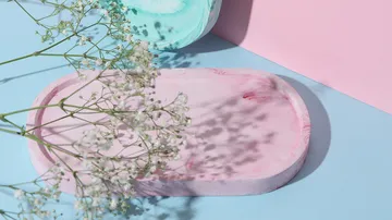 Rosa Tablett mit Blumen auf pastelliger Oberfläche.