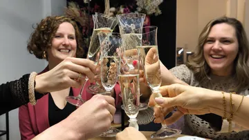 Menschen stoßen mit Sektgläsern an, lächeln drinnen.