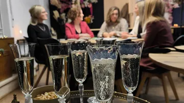 Sektgläser auf Tisch mit Frauen im Gespräch.